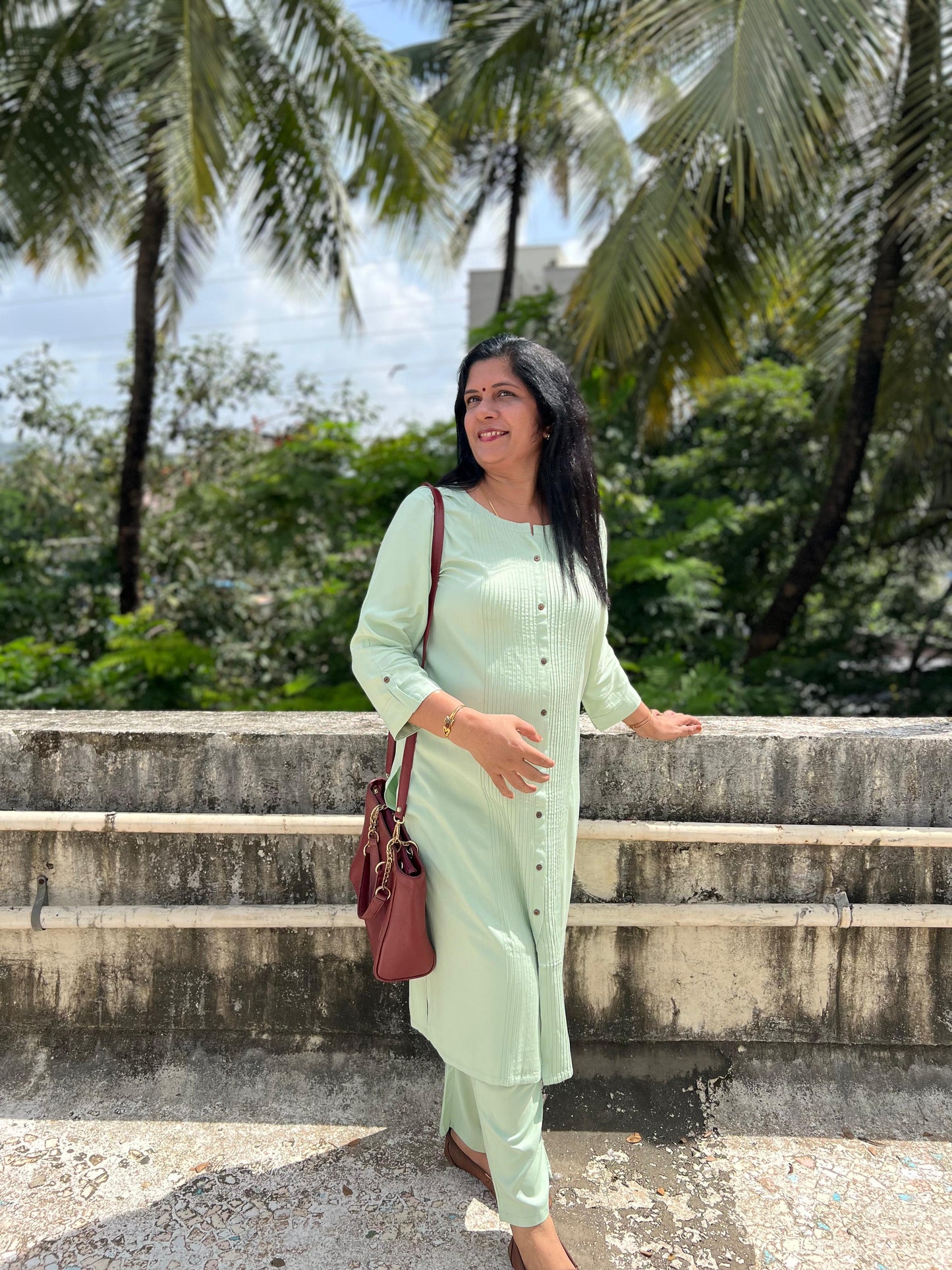 Woman in a light green outfit standing outdoors with palm trees in the background
