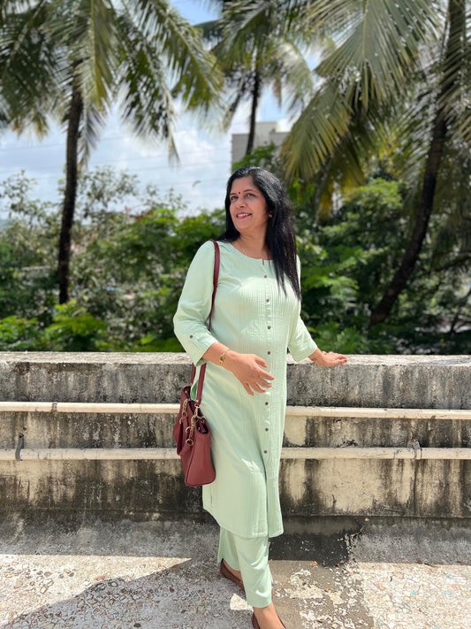 Woman in a light green outfit standing outdoors with palm trees in the background