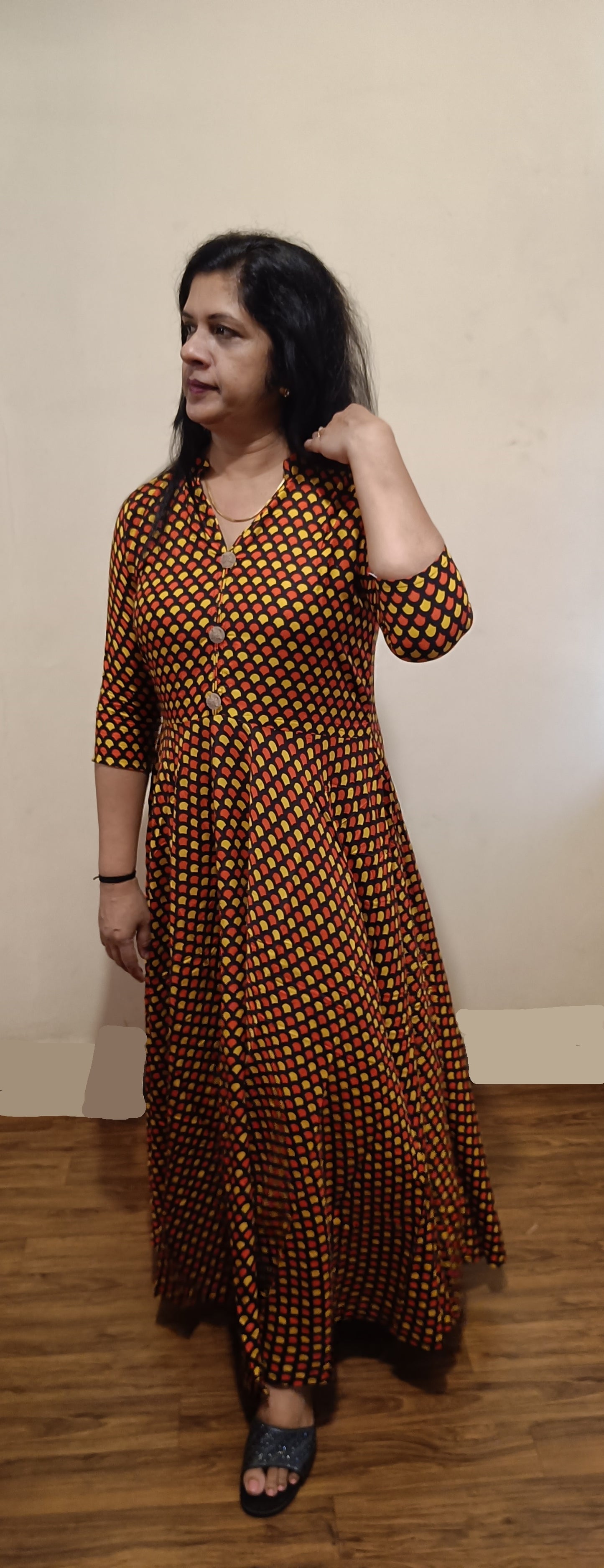 Woman wearing a long brown dress with a pattern against a plain background