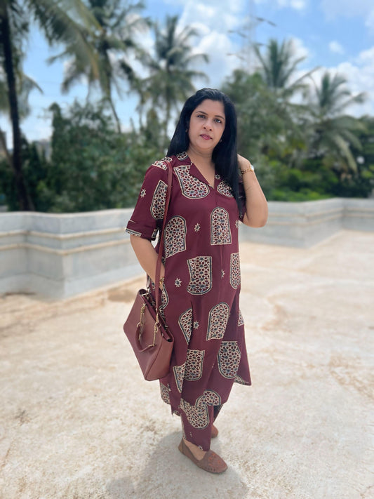 Woman in a maroon patterned dress standing outdoors with palm trees in the background